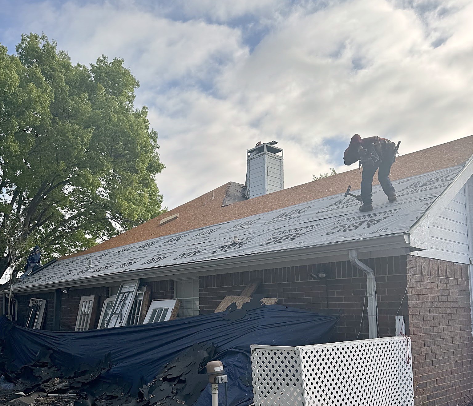 A roofer with a nail gun working along the ridge while the rest of the roof is stripped back to underlayment