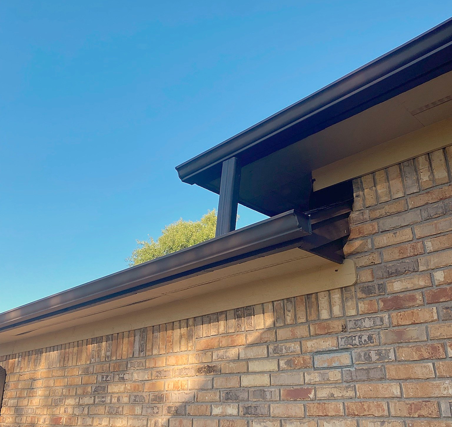 A dark gutter and downspout running along the eaves of a brick house