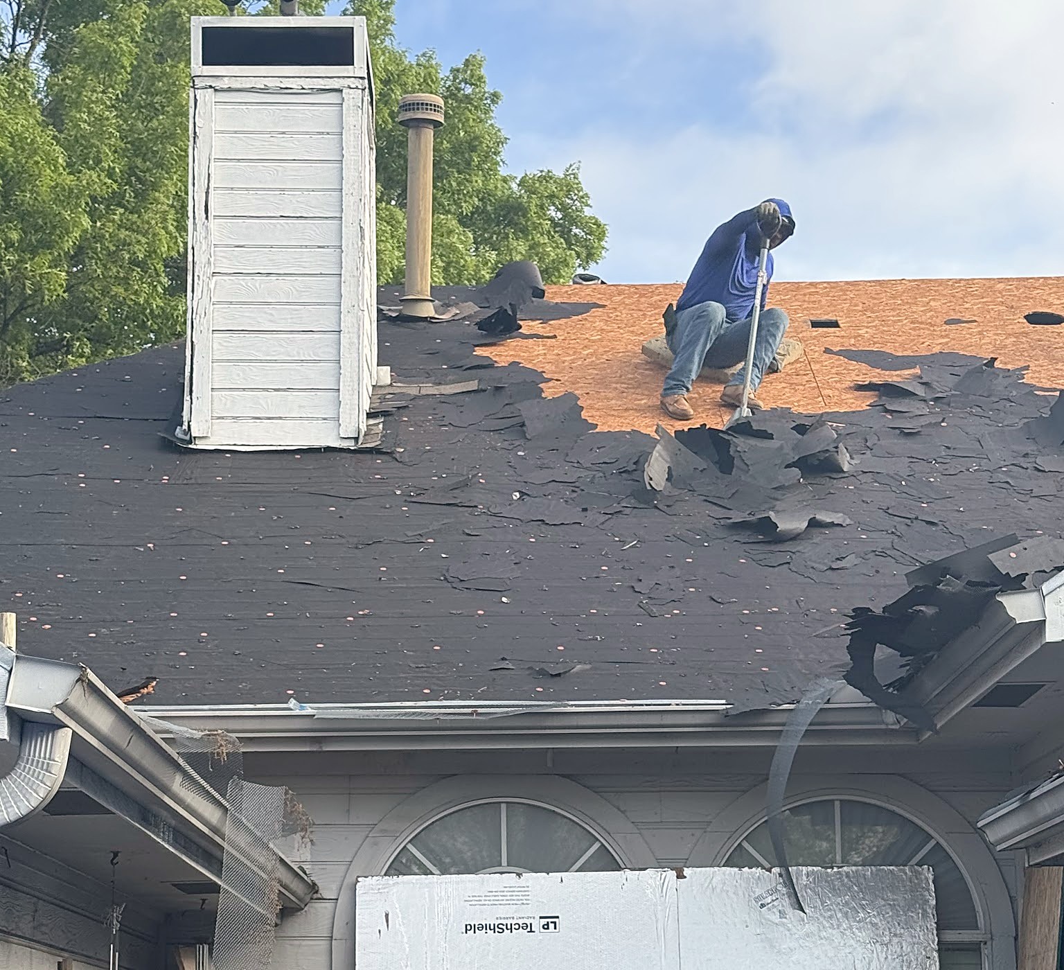 A roofer scraping the old shingles off a roof down to the bare decking