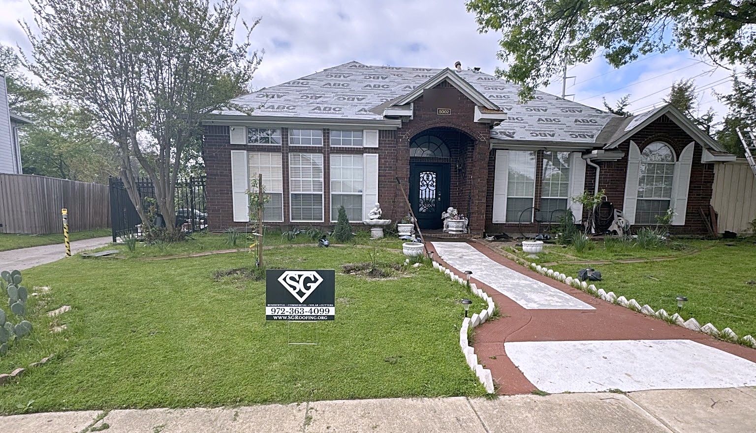 A brick house part way through a re-roof, underlayment down across the whole roof and an SG Roofing sign in the front yard
